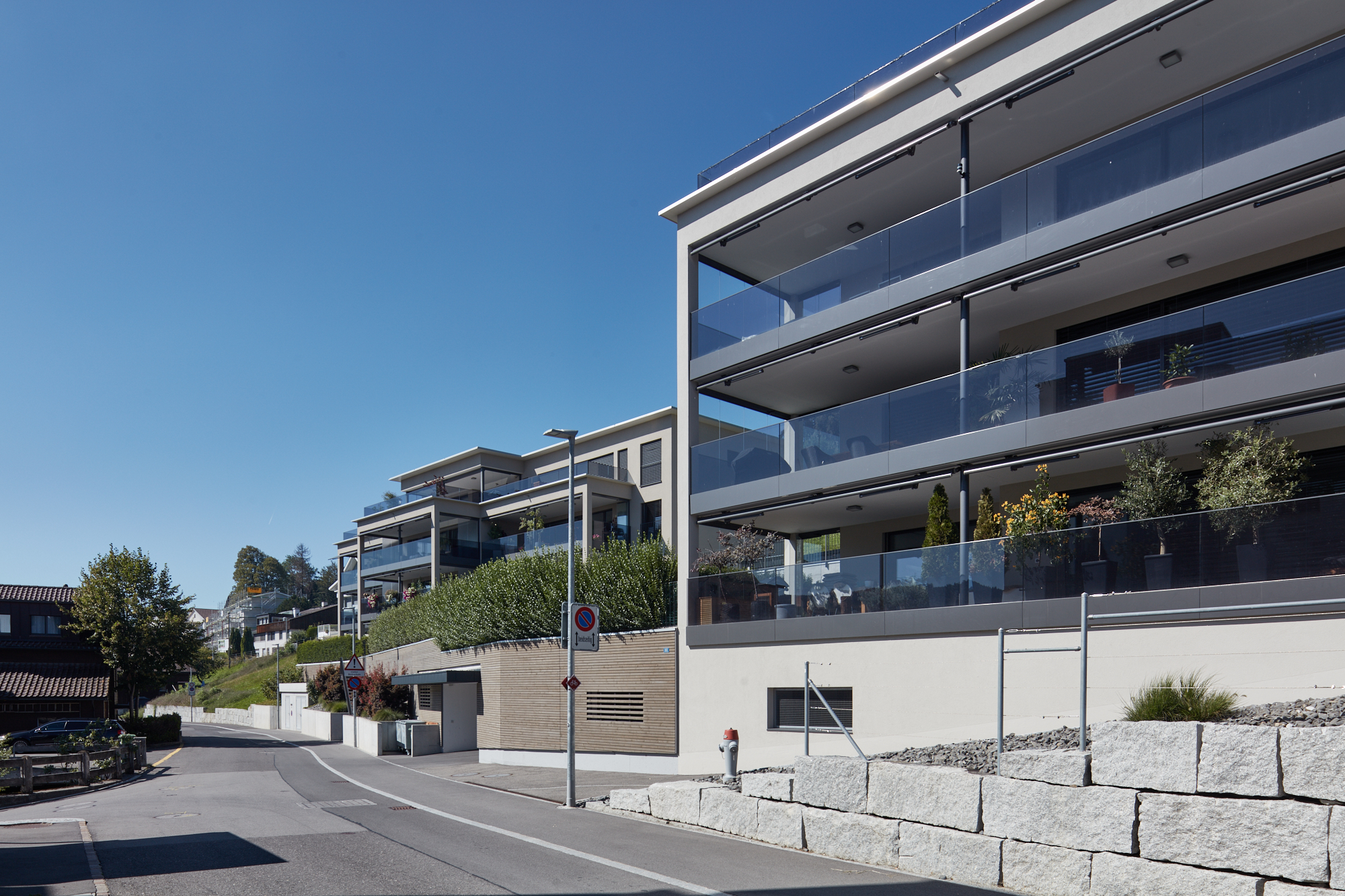 Strassenansicht der Terrassenhäuser mit Glasbrüstungen und Natursteinmauer