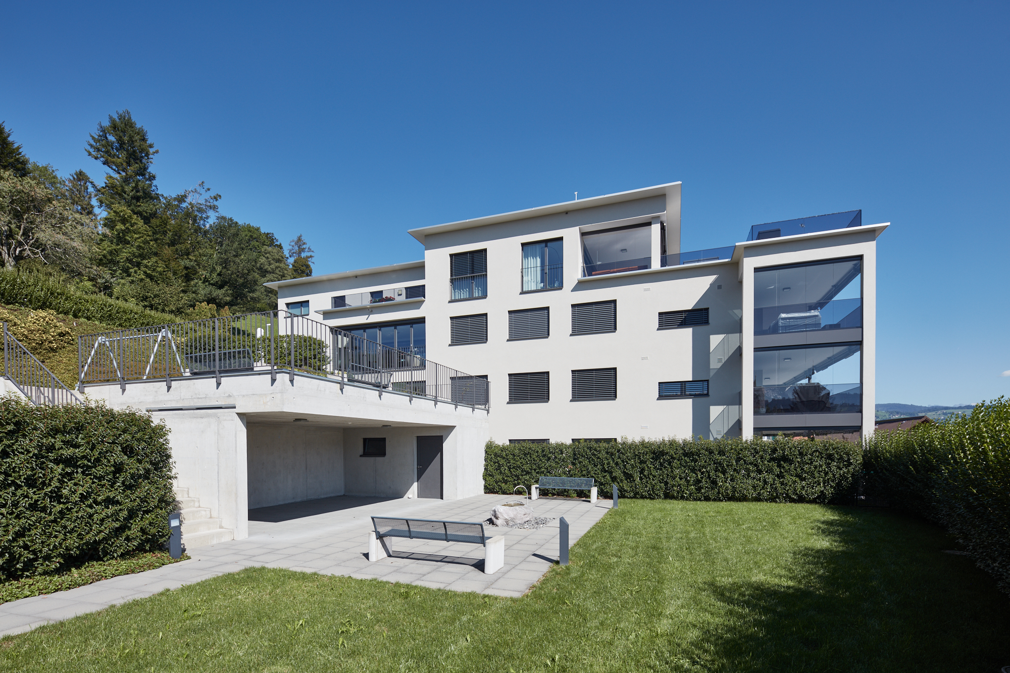 Rückseite der Wohnanlage mit Betonterrasse, Sitzbänken und Rasenfläche