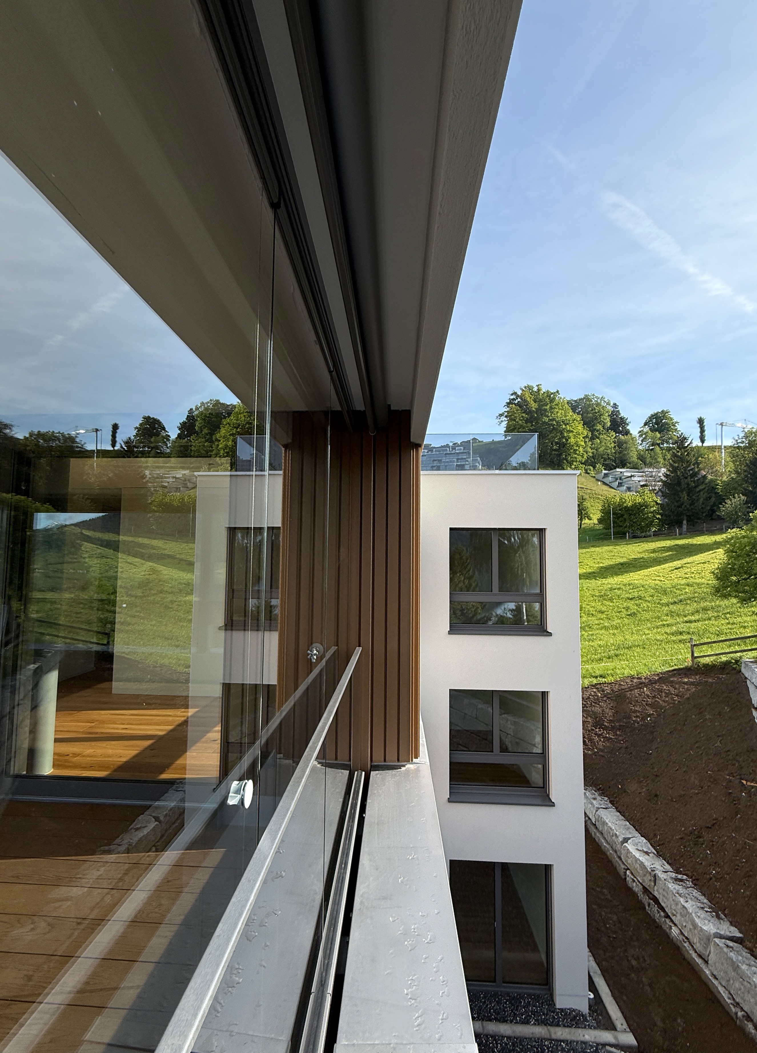 Rothusweg — Blick entlang der Glasbrüstung auf Holzlamellen und die helle Putzfassade